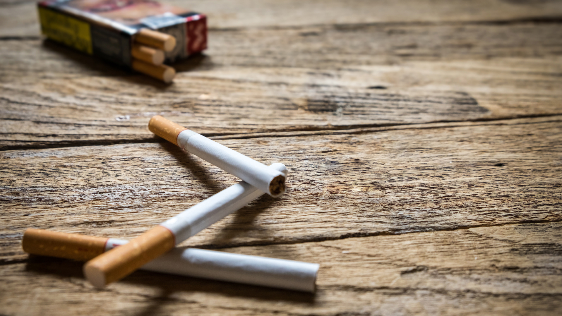 Expired cigarettes on a wooden table in front of an open pack of cigarettes